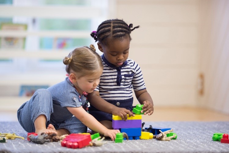 Two children building a block tower while also including other toys